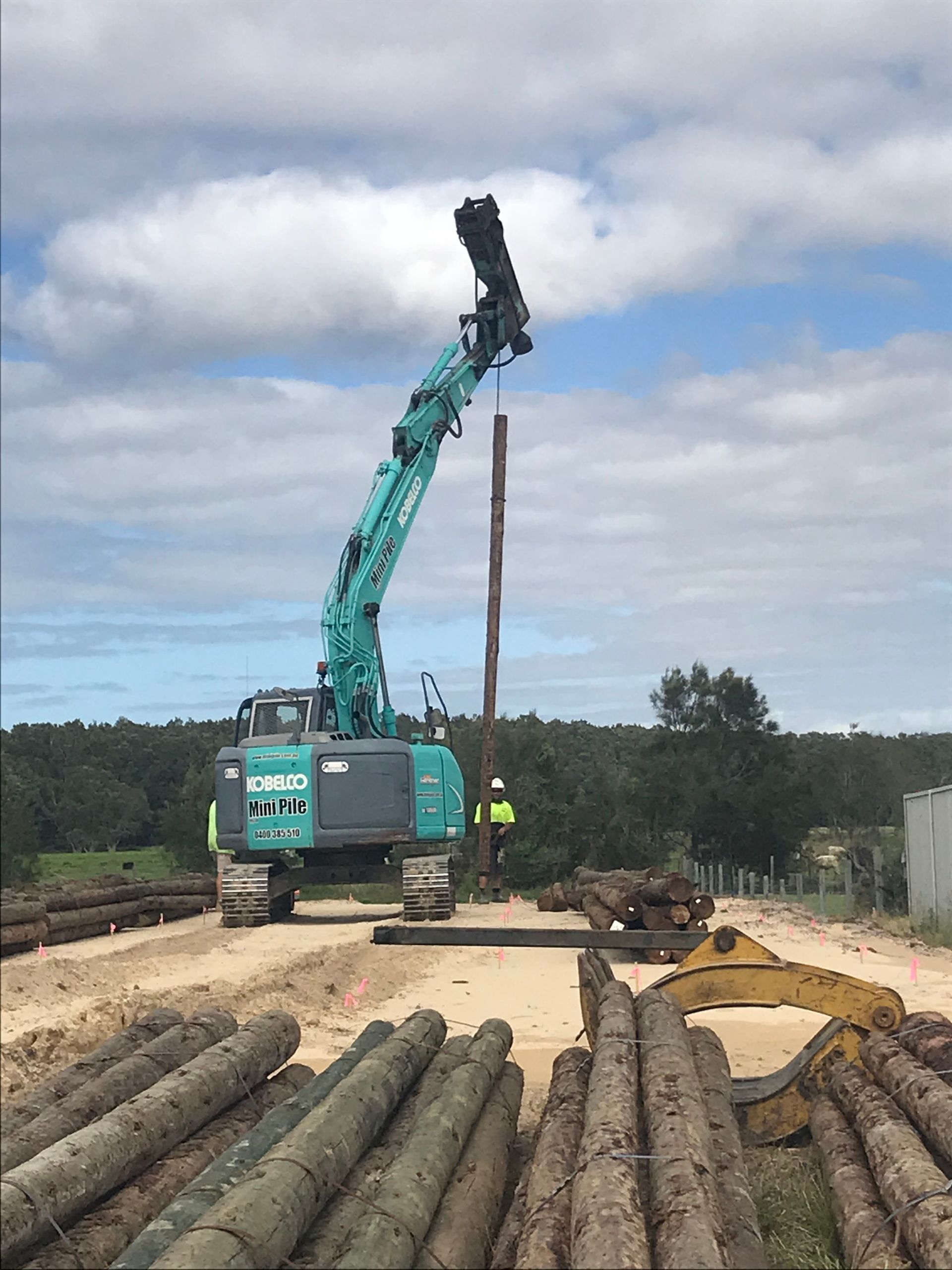 Excavator Driving a Wooden Piling Into the Ground at a Construction Site — Keystone Property Solutions In Waratah, NSW