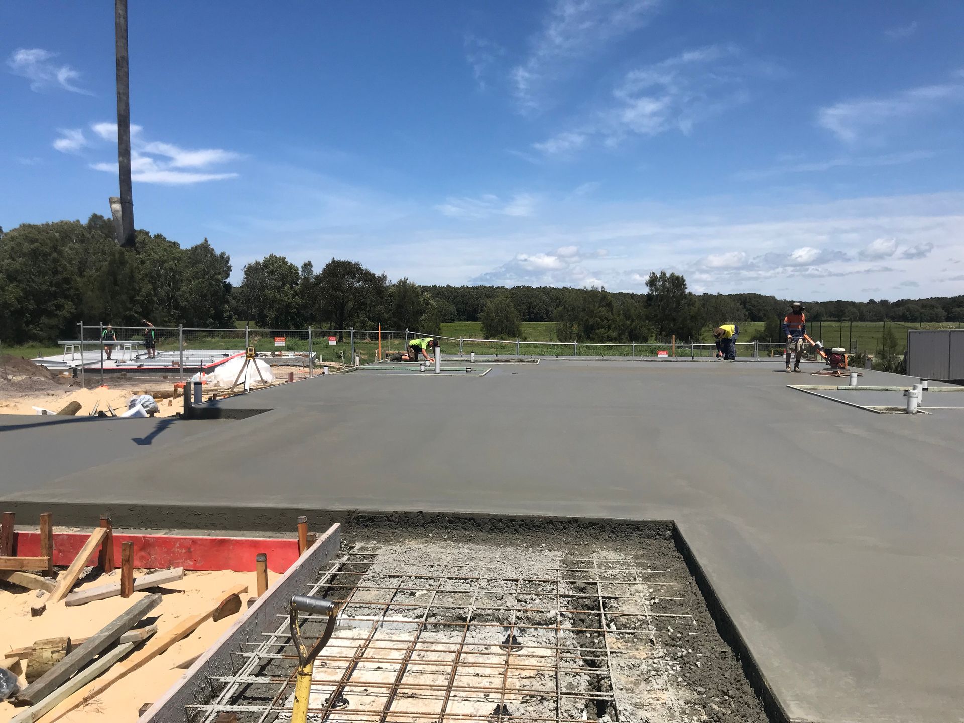 Concrete slab being poured at a construction site on a sunny day. Workers in the background.