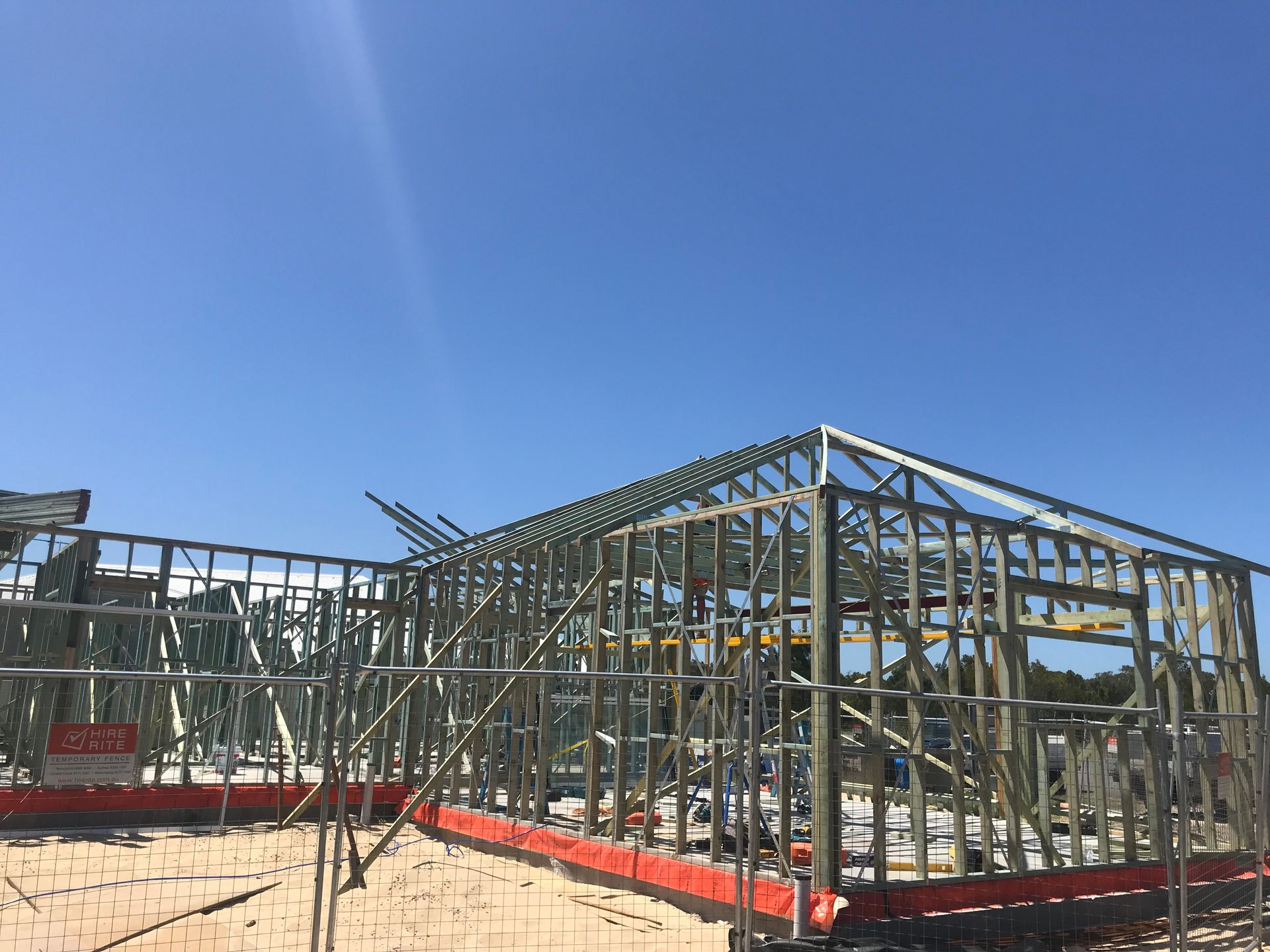 Metal framing of a house under construction against a clear blue sky.
