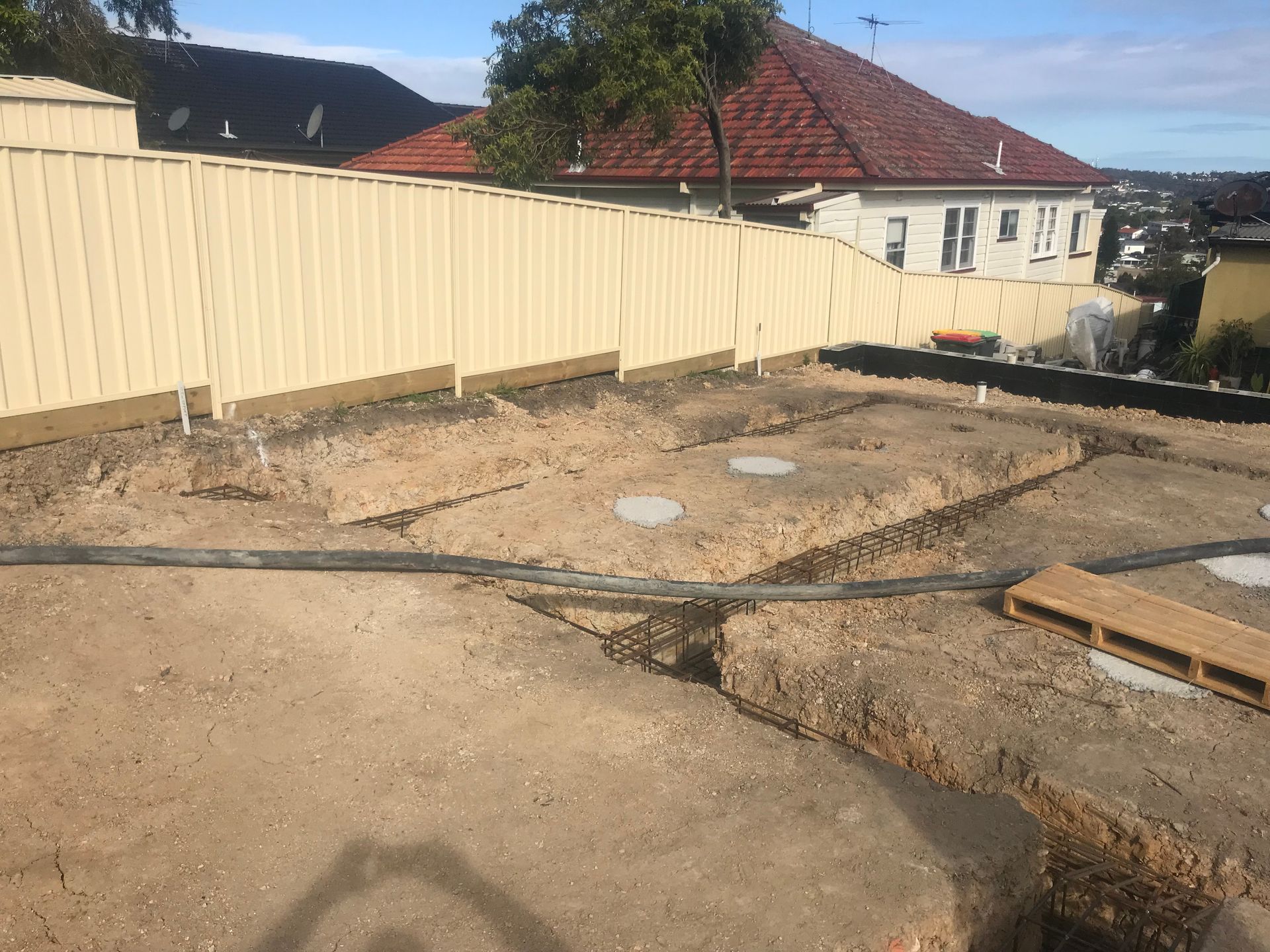 Excavation Site With Trenches and Concrete Footings, Bordered by a Beige Fence — Keystone Property Solutions In Waratah, NSW