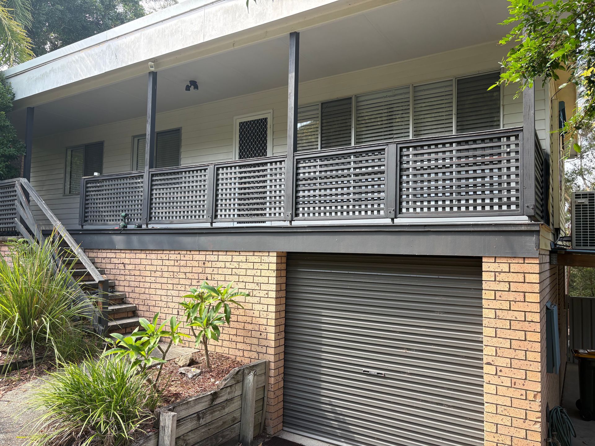 Two-story house with a balcony and a garage. Brick and gray exterior with a wooden railing and stairs.