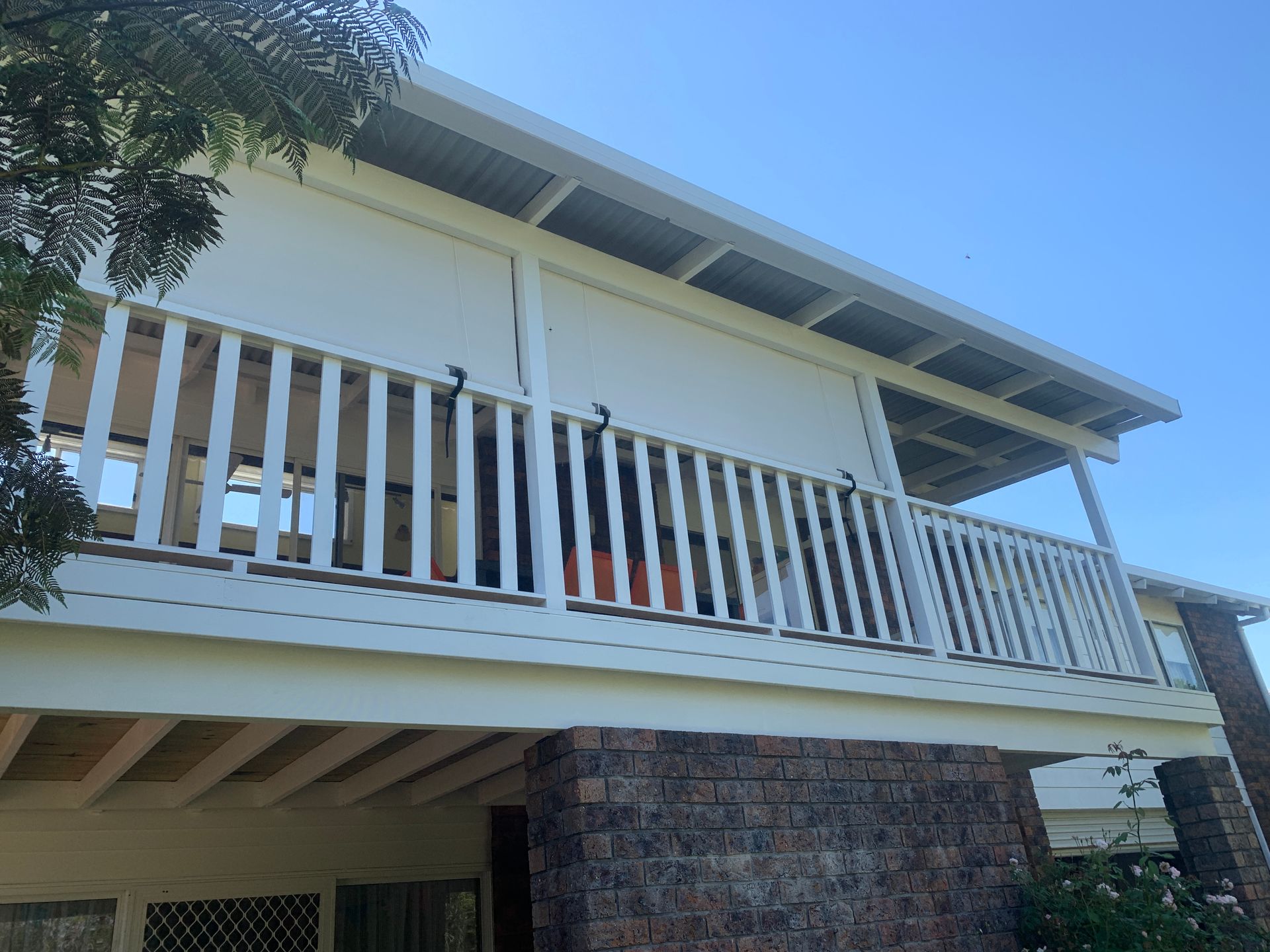 Two-story house with a white balcony and beige shade rolled down, under a blue sky.