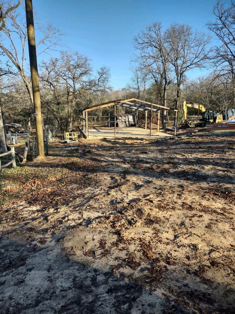 A building is being built in the middle of a dirt field surrounded by trees.