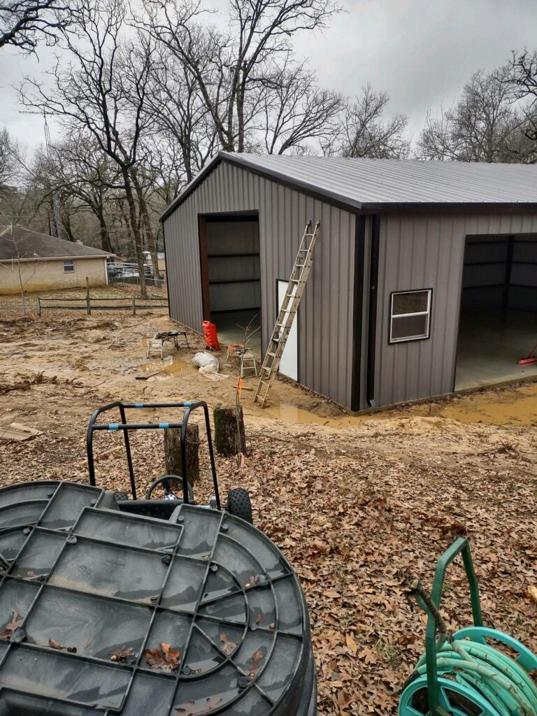 A large metal building is being built in the middle of a dirt field.