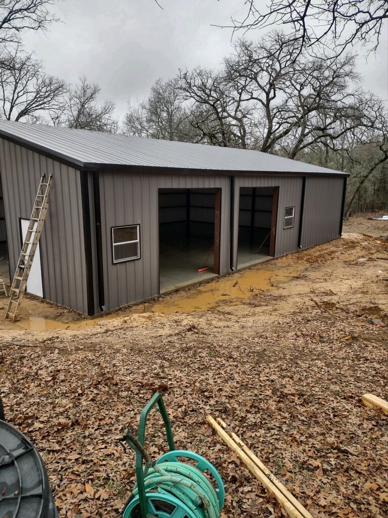 A large metal building is being built in the middle of a dirt field.