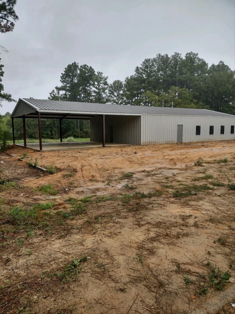 A large metal building with a canopy is sitting in the middle of a dirt field.