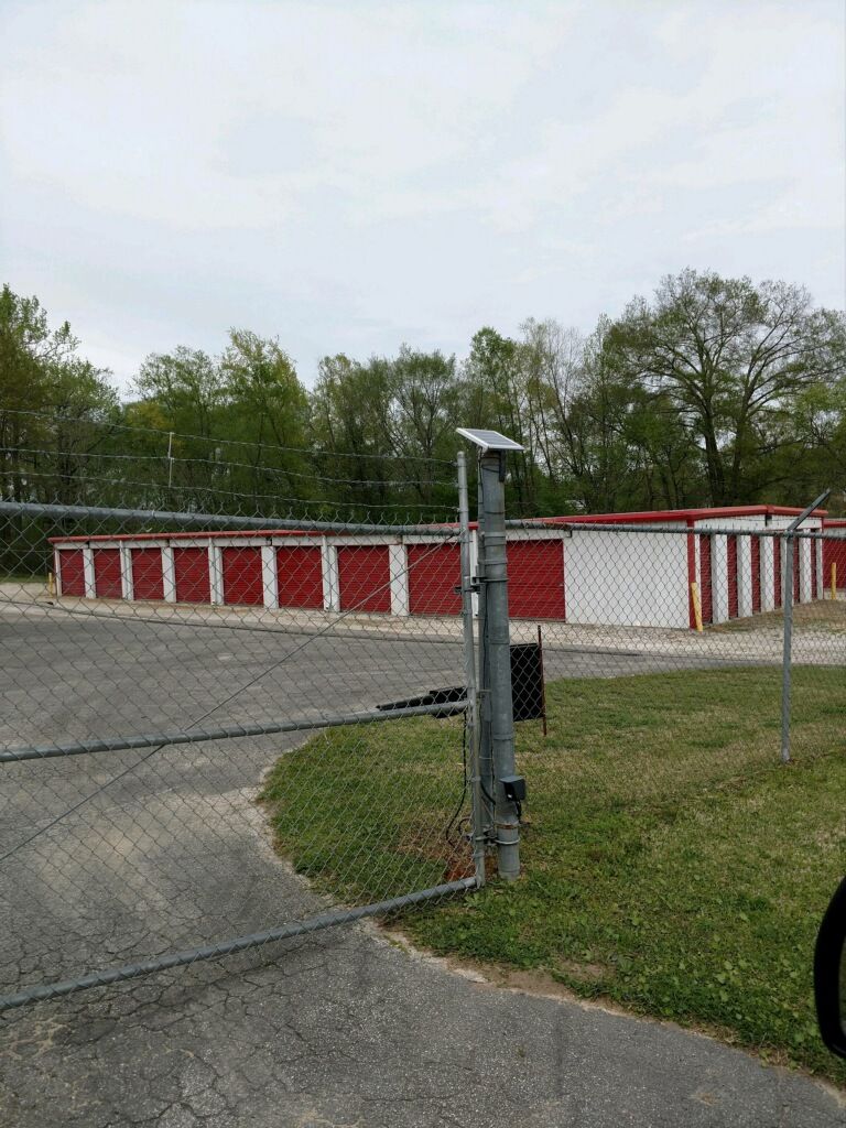 A chain link fence surrounds a parking lot with red and white storage units.
