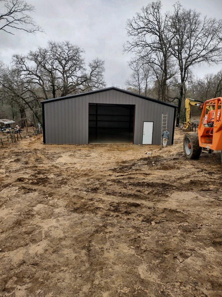 A large metal building is being built in the middle of a dirt field.