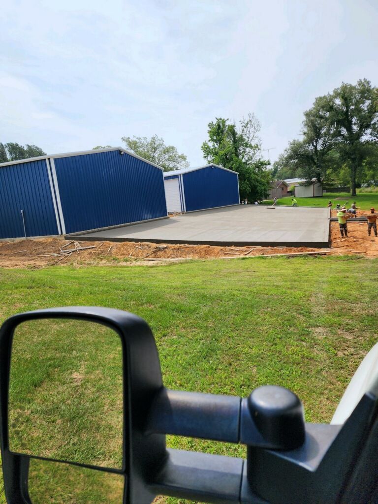 A truck is parked in a grassy field with a blue building in the background.