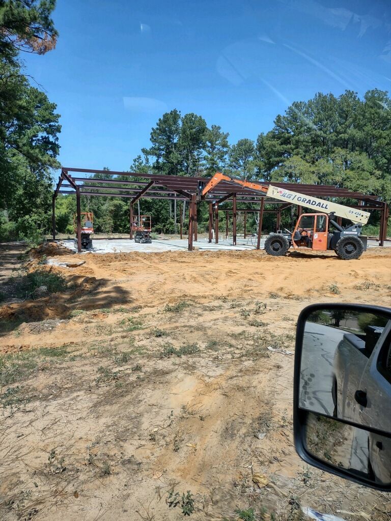 A truck is driving down a dirt road next to a building under construction.