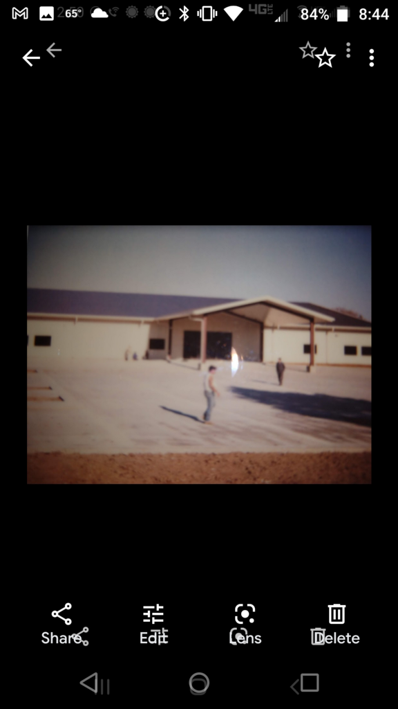 A phone screen shows a picture of a man standing in front of a building