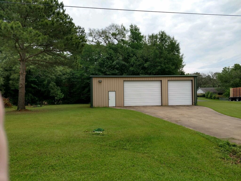 A garage with two white garage doors is in the middle of a lush green field.