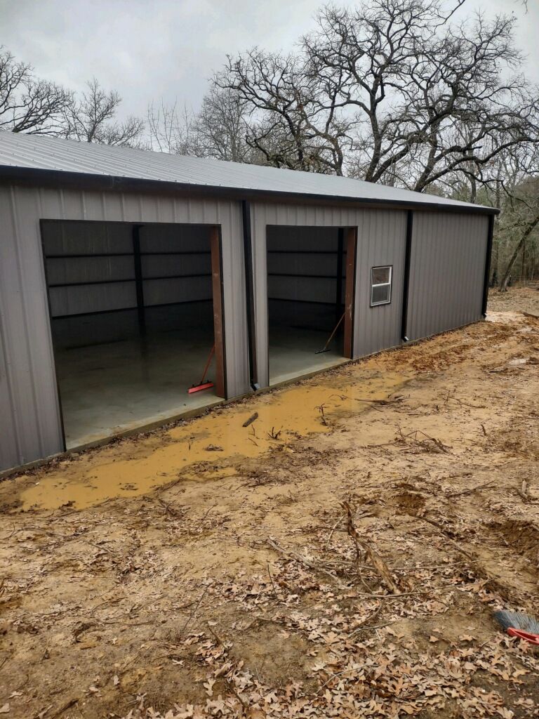 A metal garage is sitting in the middle of a dirt field.