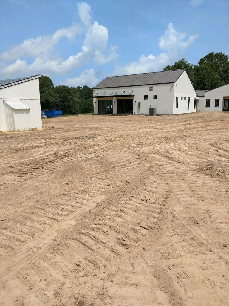 A large white house is sitting in the middle of a dirt field.