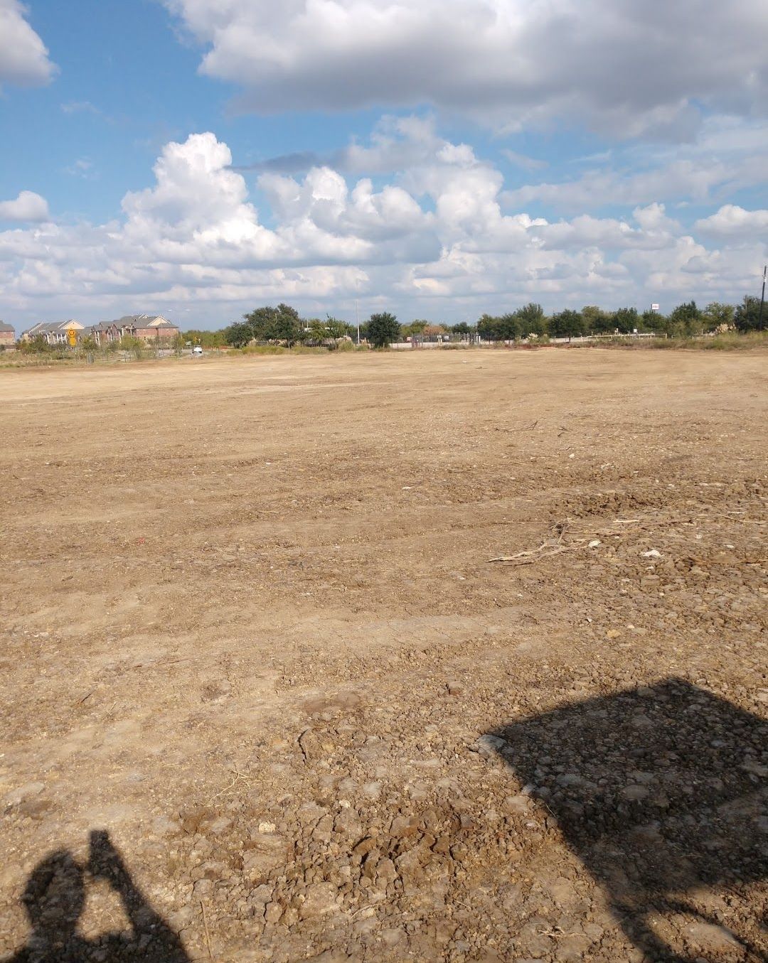 A shadow of a person is cast on a dirt field
