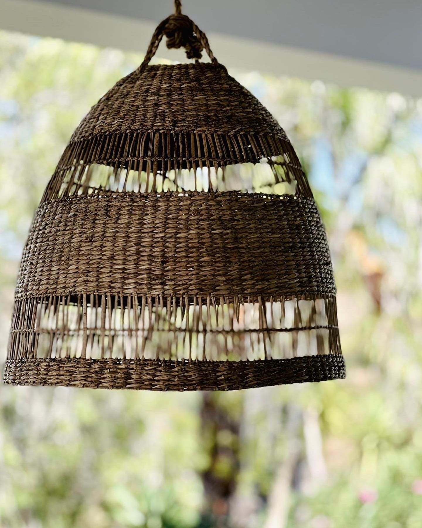 Een rieten lamp die aan het plafond hangt met bomen op de achtergrond