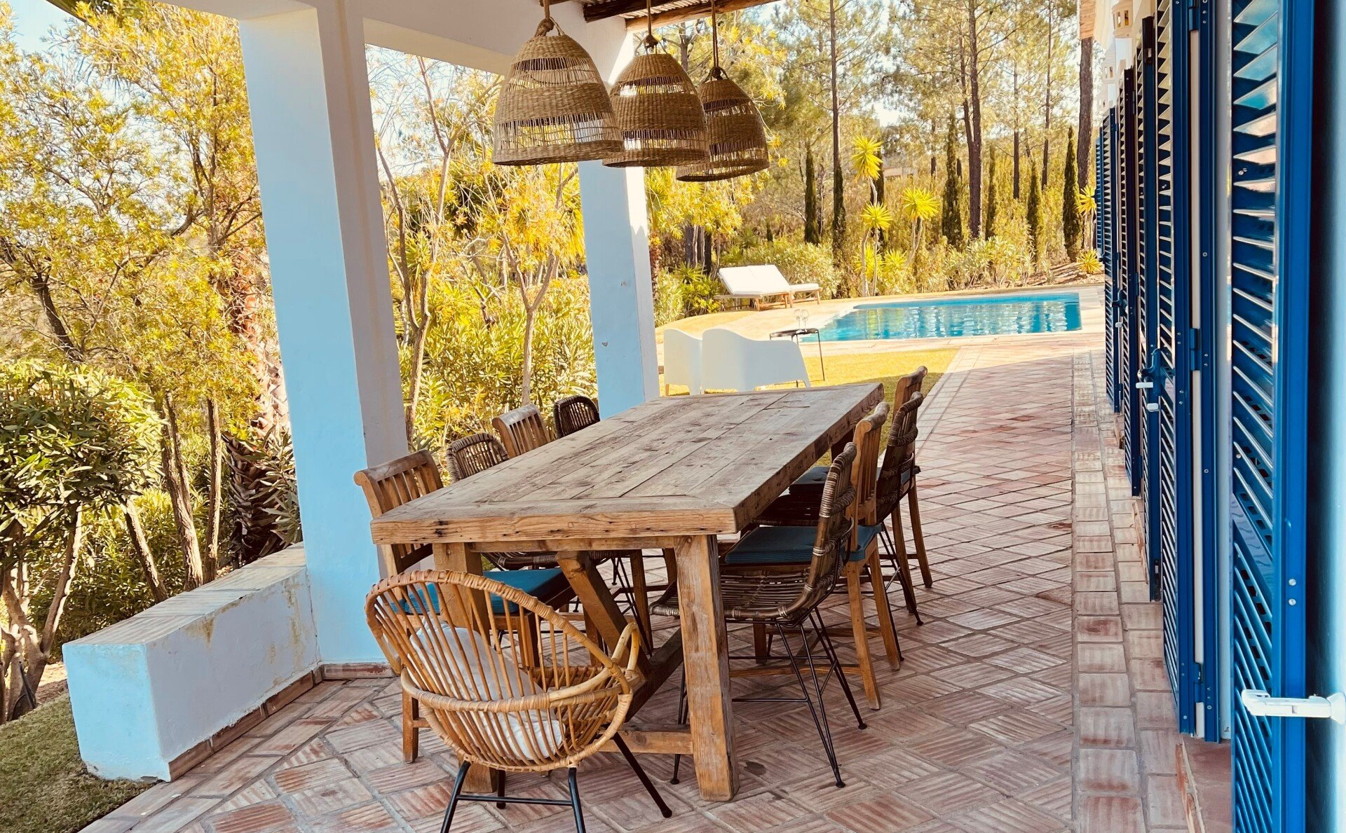 Een grote houten tafel en stoelen op een terras naast een zwembad.