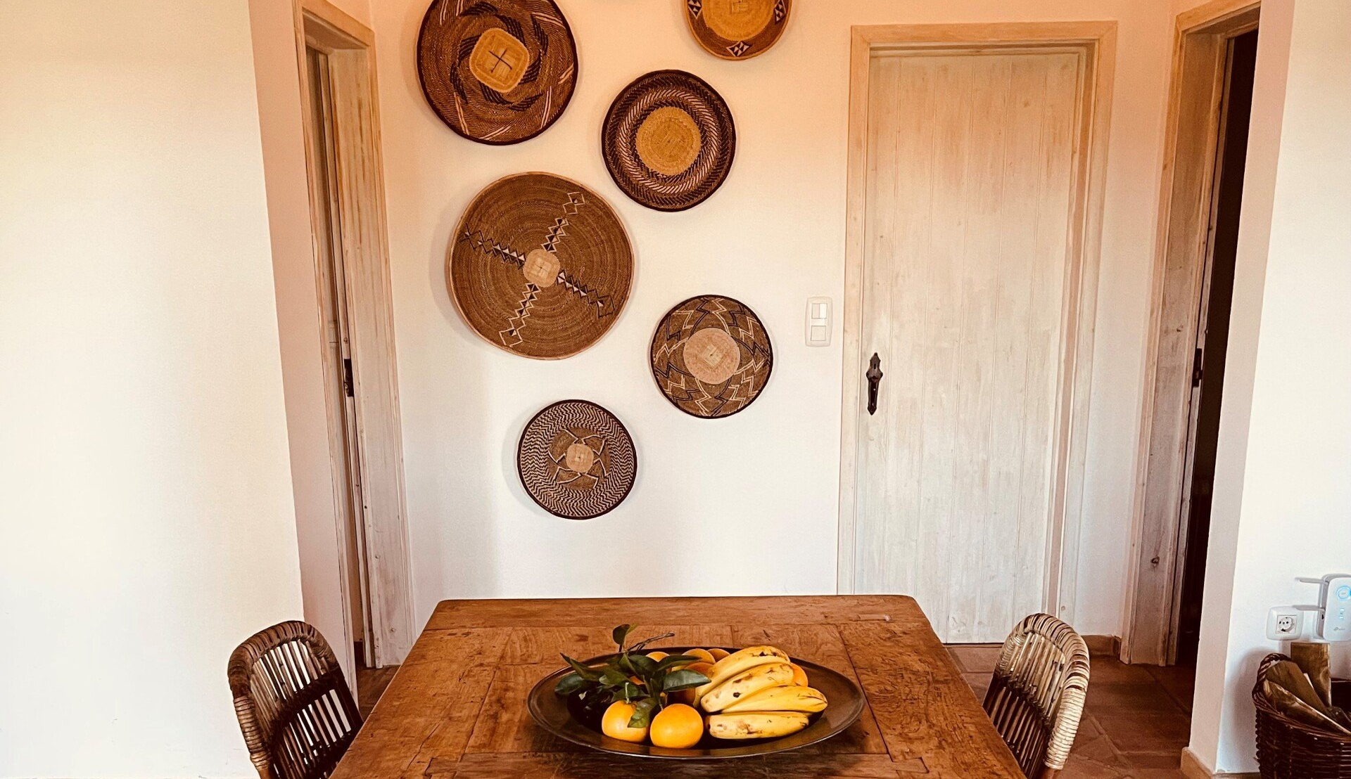 Een eetkamer met een houten tafel, stoelen en een schaal met fruit erop.