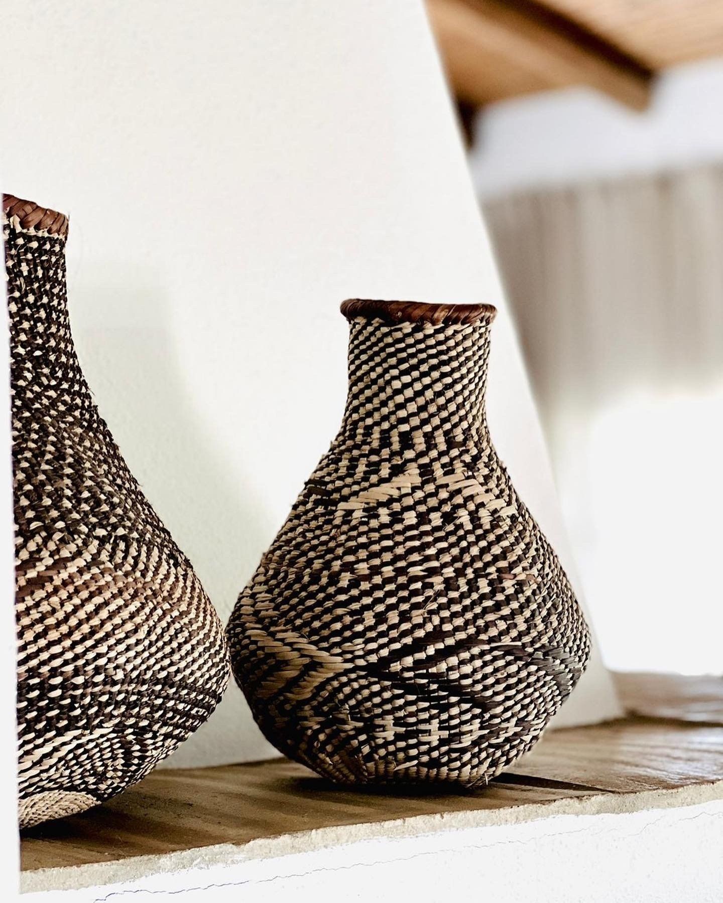 Two wicker vases are sitting on a wooden shelf