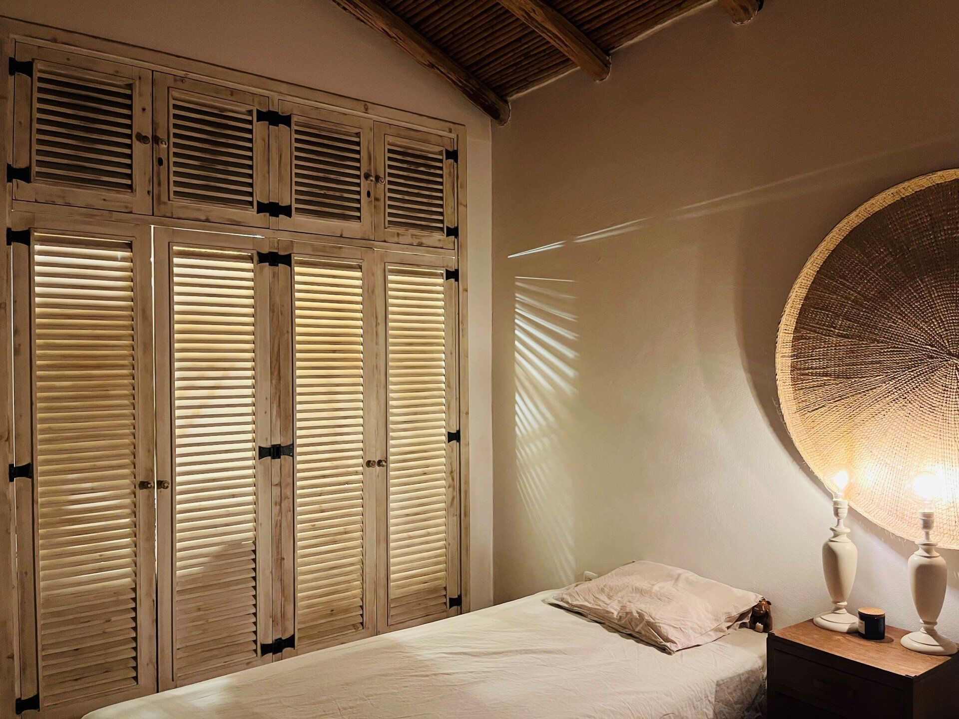 Een slaapkamer met een bed, nachtkastje, lamp en kast.