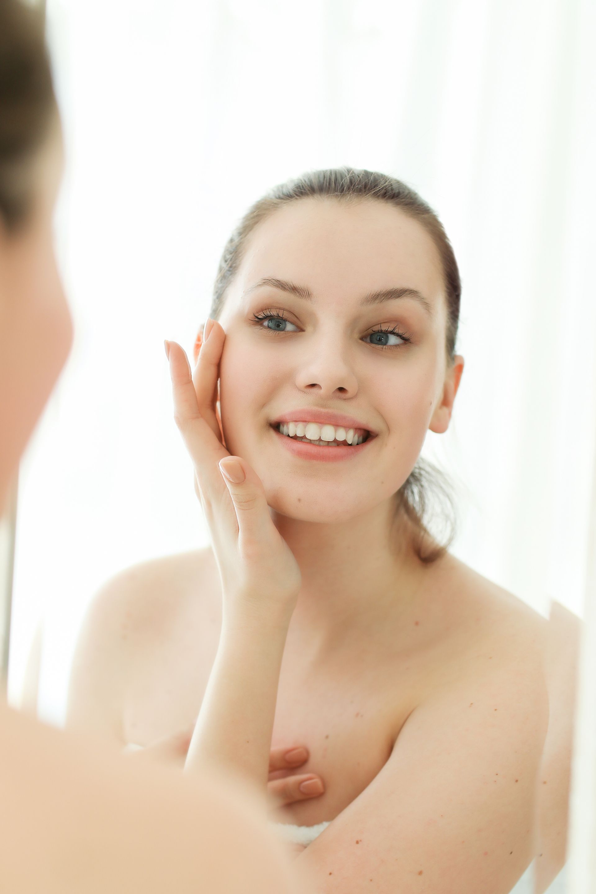 A woman is looking at her face in the mirror.