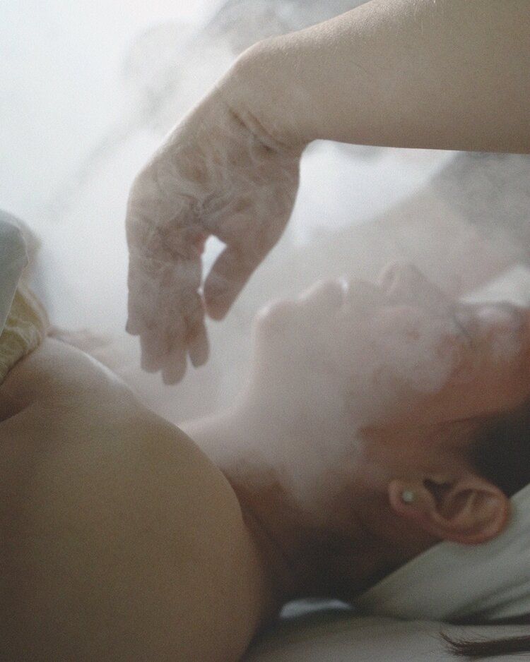 A woman is laying on a bed with steam coming out of her face.