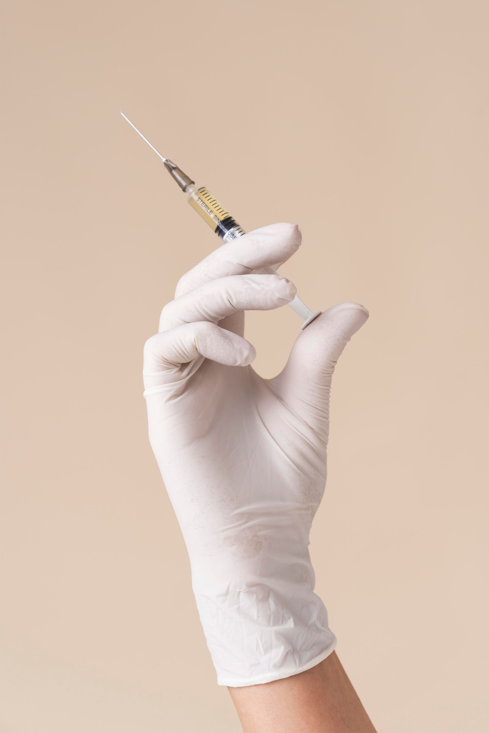 A hand in a white glove is holding a syringe.