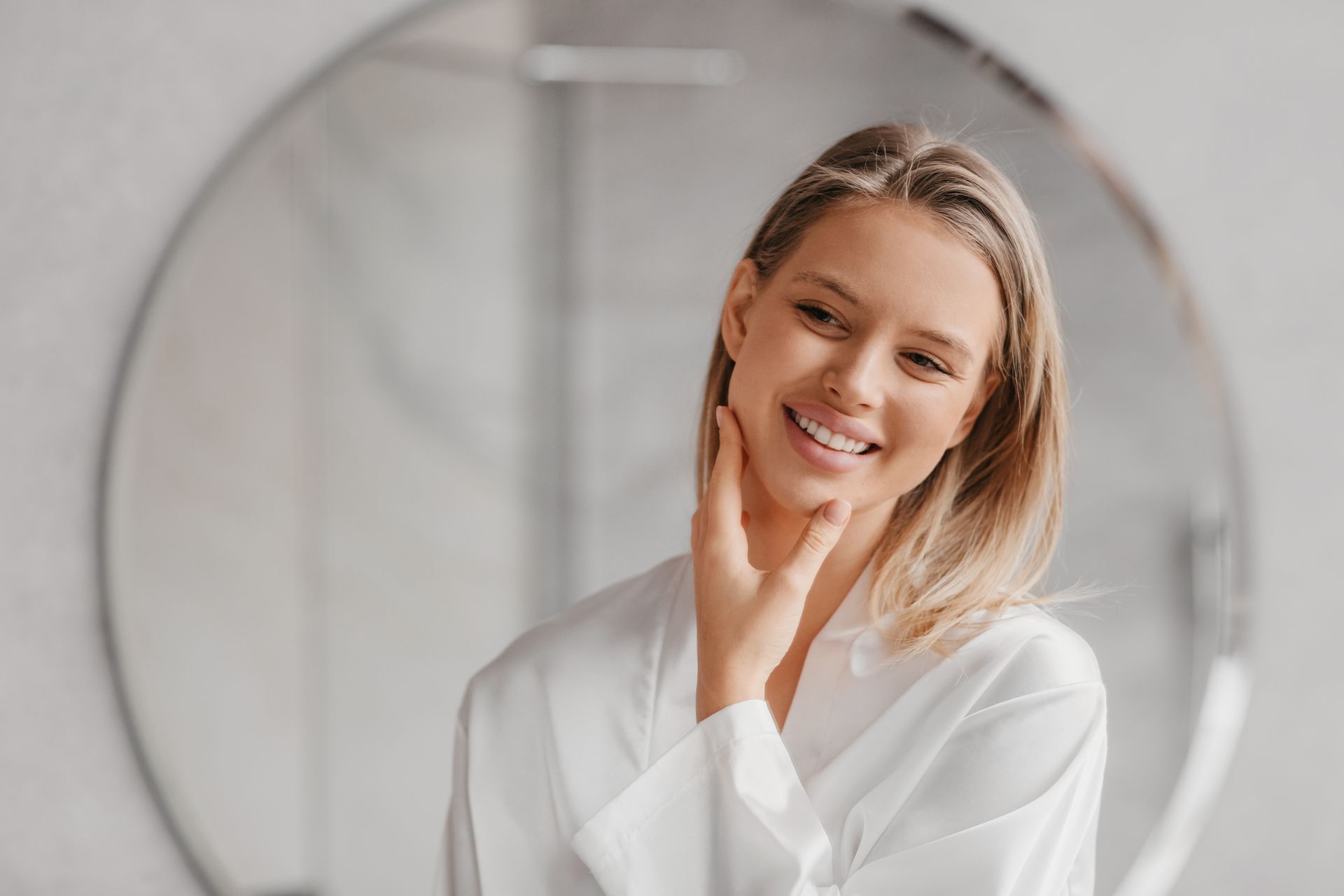 A woman is touching her face in front of a mirror.