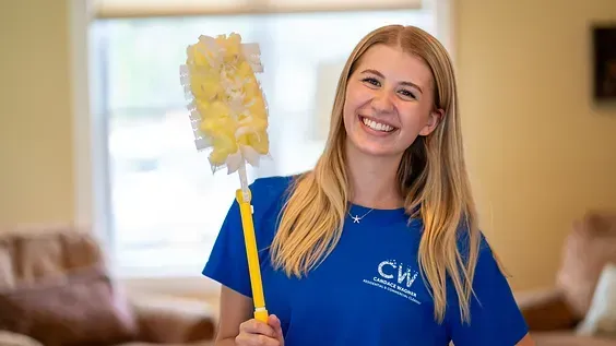 A woman in a blue shirt is holding a mop and smiling.