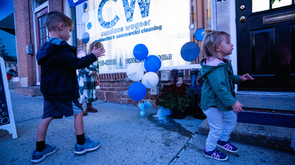 A boy and a girl are standing in front of a store with blue balloons.