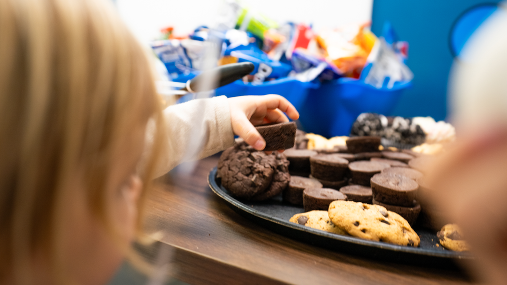 A little girl is reaching for a cookie from a tray of cookies.