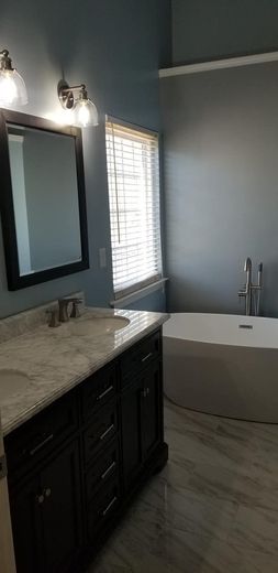 A bathroom featuring a dark wood vanity with a marble countertop, a wall mirror, a window with blinds, and a soaking tub.
