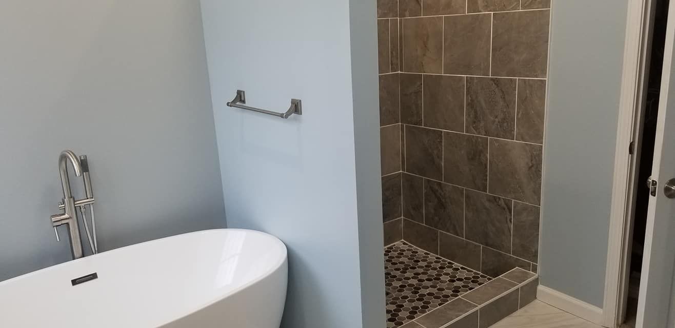 A modern bathroom featuring a white freestanding soaking tub next to a tiled walk-in shower with a pebble floor.