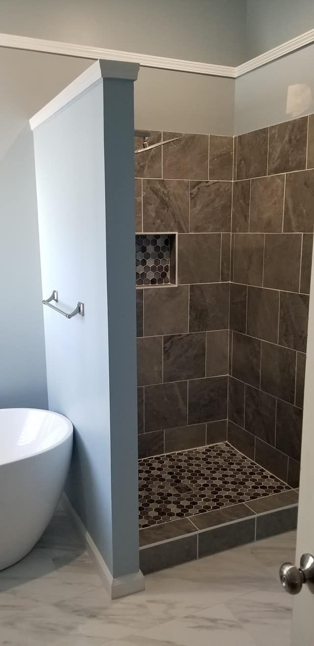 A bathroom featuring a walk-in shower with stone tile walls, a pebble floor, a small wall niche, and a freestanding tub.