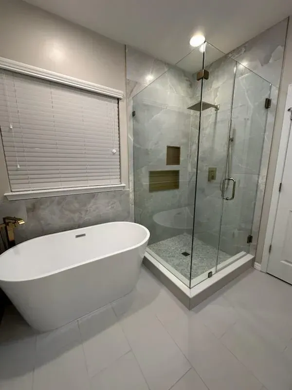 A modern bathroom featuring a white freestanding bathtub next to a glass-enclosed shower with tiled walls.