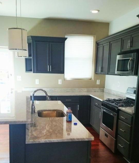 A kitchen with dark cabinets, light granite countertops, a stainless steel oven, and a sink on the island.