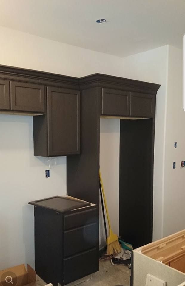 Dark brown kitchen cabinets installed along a white wall, including an upper cabinet over a refrigerator opening.