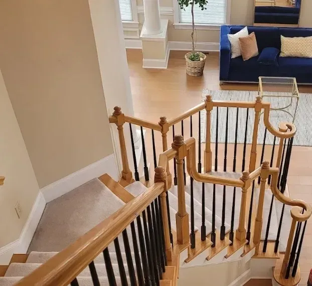 A high-angle view of a carpeted staircase with wood railings and black spindles leading down to a living room with a sofa.