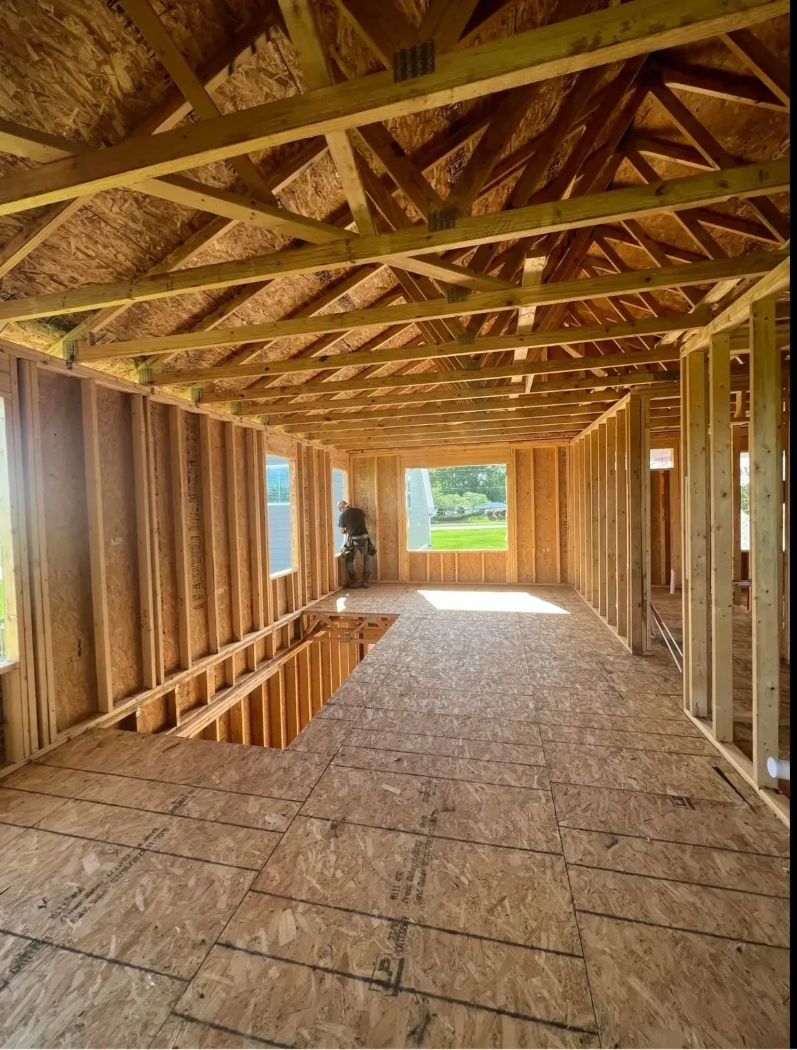 Interior view of a wooden house framing project with a subfloor, wall studs, and exposed roof trusses under construction.