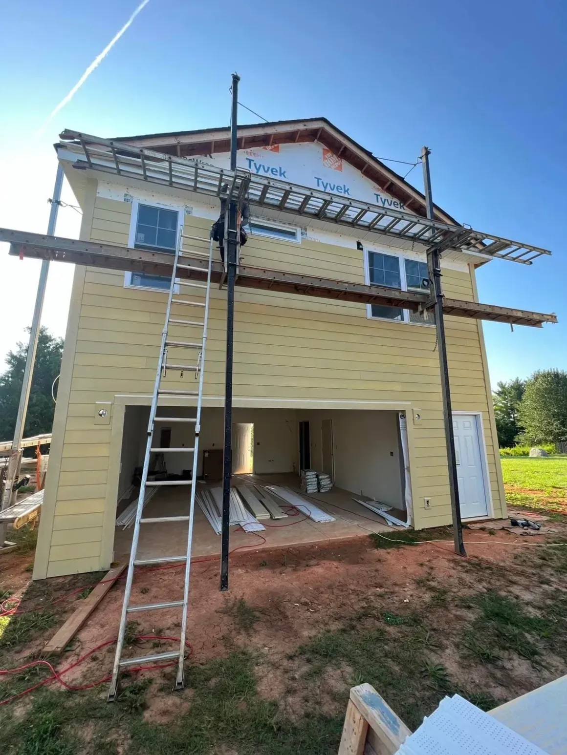 A yellow two-story house under construction with exterior scaffolding, a tall ladder, and exposed wood siding.