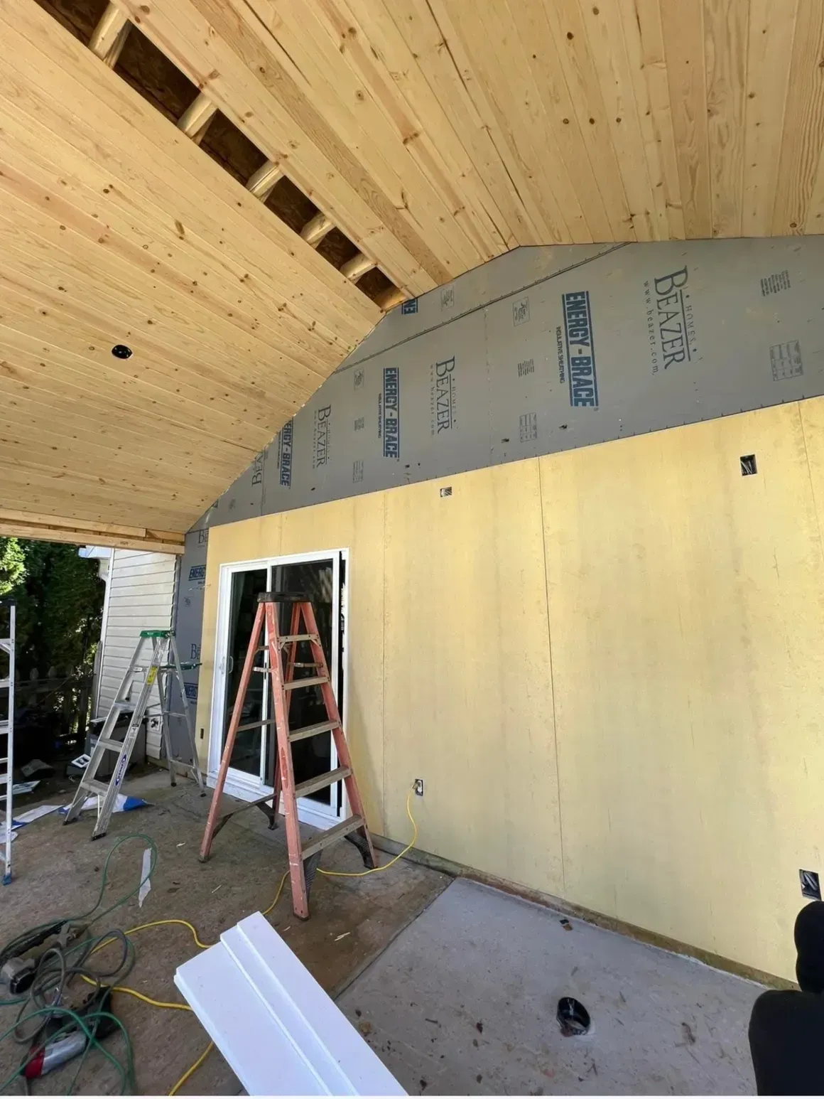 A construction site showing a wall with yellow insulation panels and a grey upper section, with a ladder near a doorway.