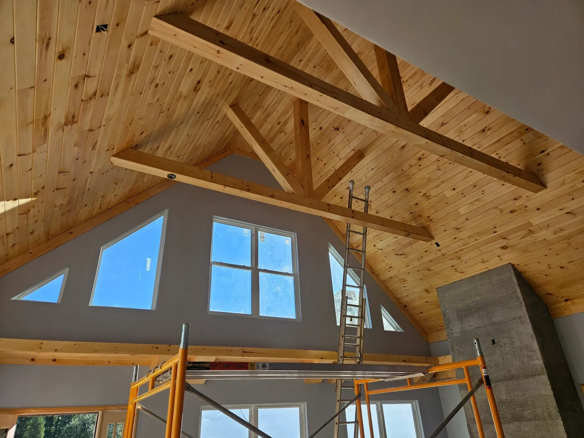Interior view of a room under construction with vaulted wood-paneled ceilings, timber beams, and scaffolding.