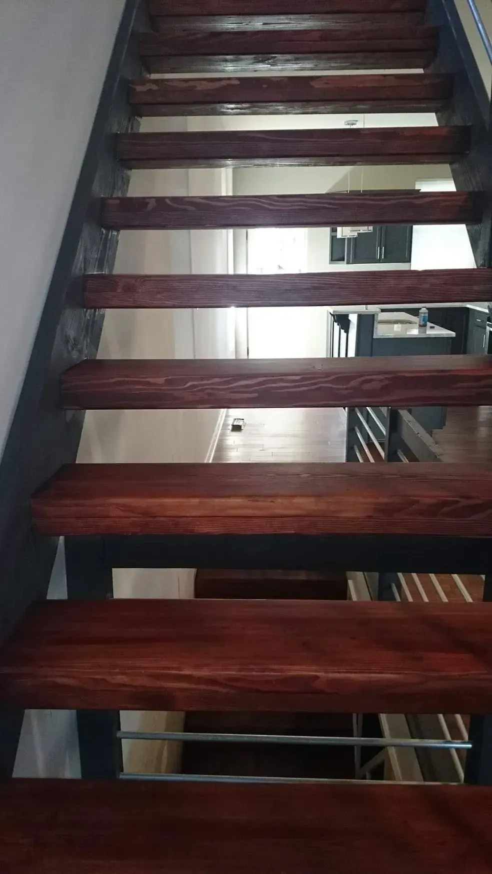 A straight wooden staircase with dark-stained treads and black supports, viewed from the bottom looking up.
