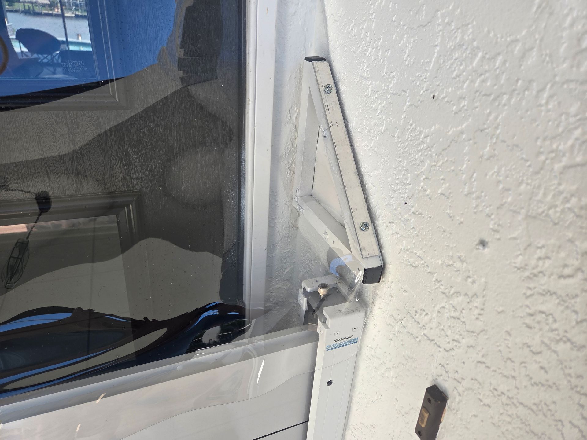 White window frame with an attached metal arm bracket on a stucco wall.