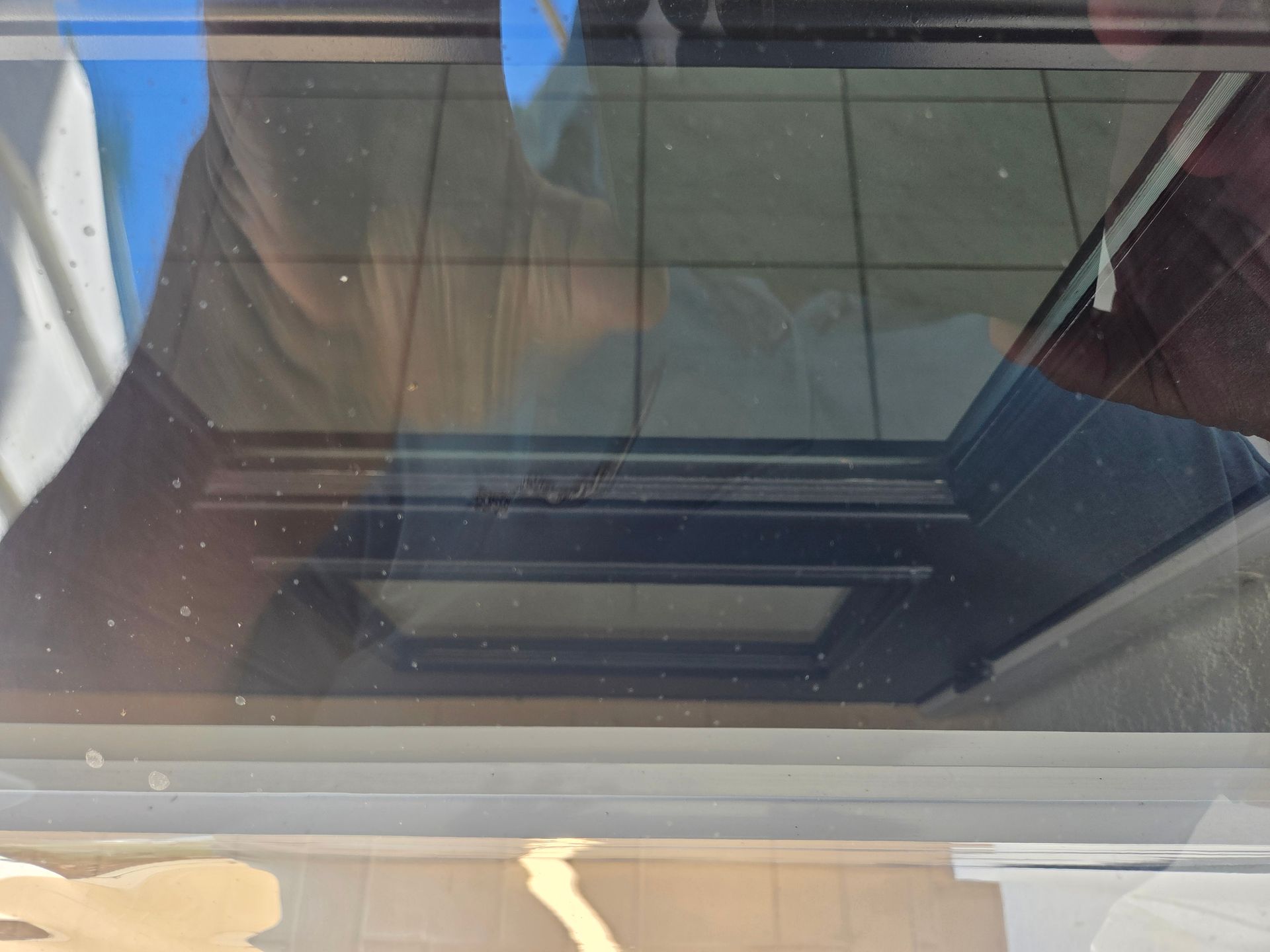 Looking through a glass window towards a dark, rectangular opening with lines, likely part of a building's structure.