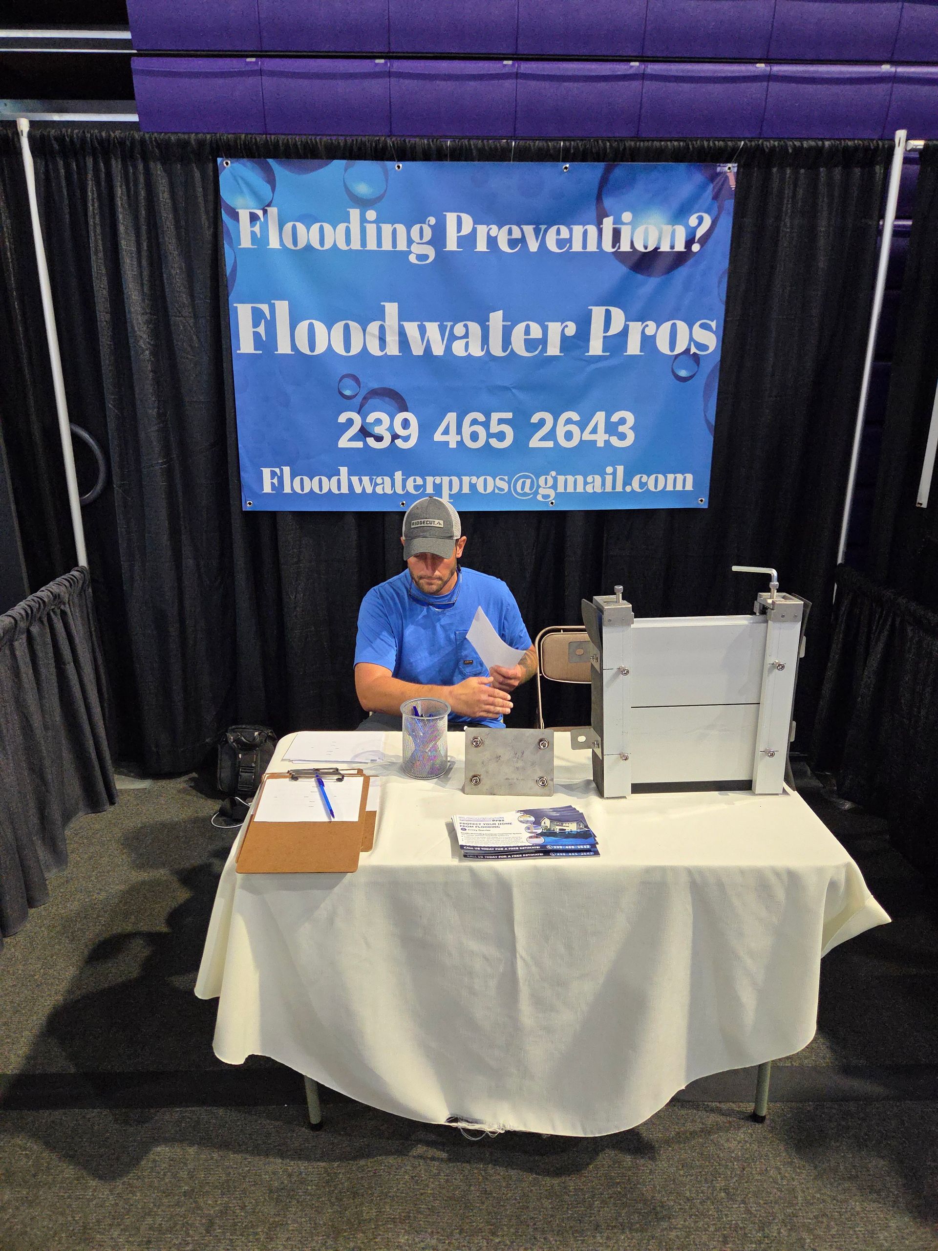 A man sits at a table in front of a sign that says floodwater pros
