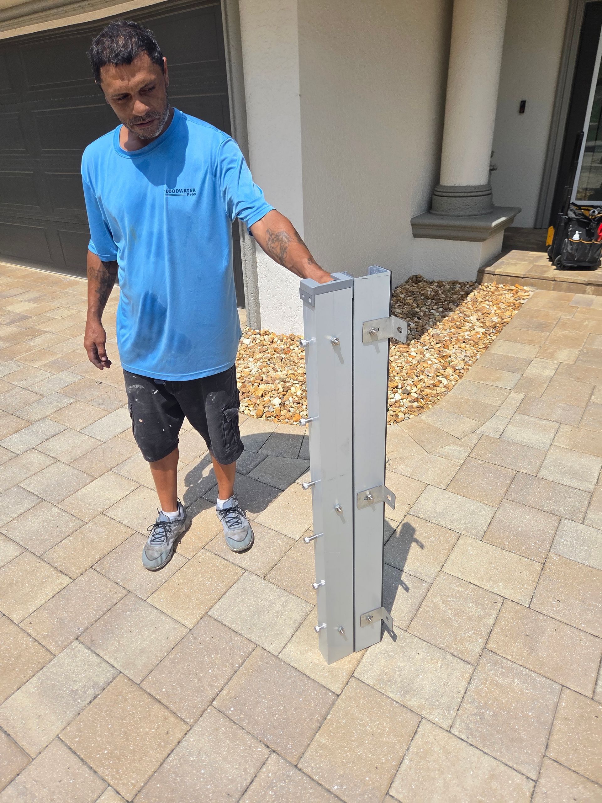 A man in a blue shirt is standing on a brick sidewalk holding a metal pole.
