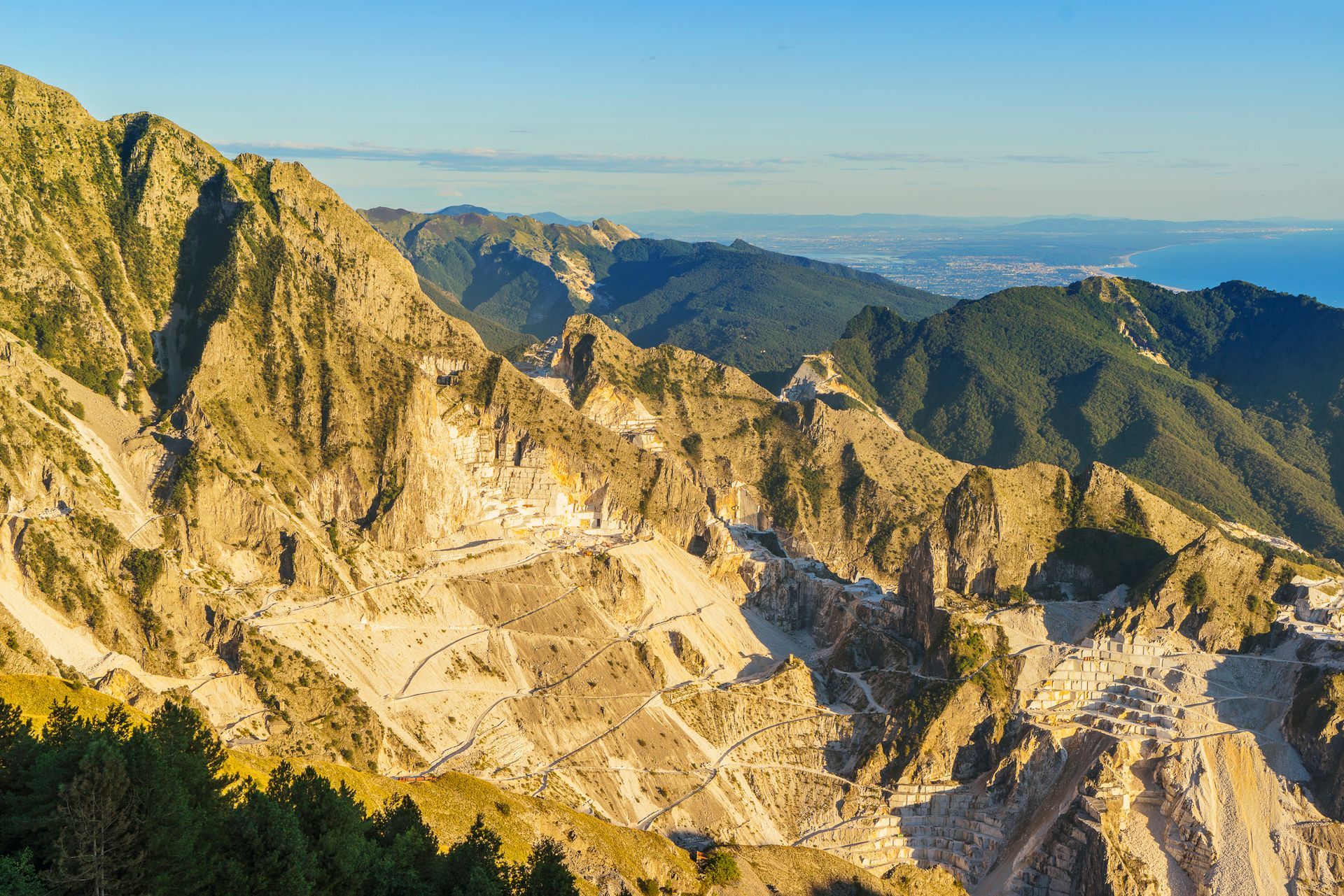 Catena montuosa con pareti rocciose esposte, diverse tonalità di marrone e verde e un cielo azzurro e terso.