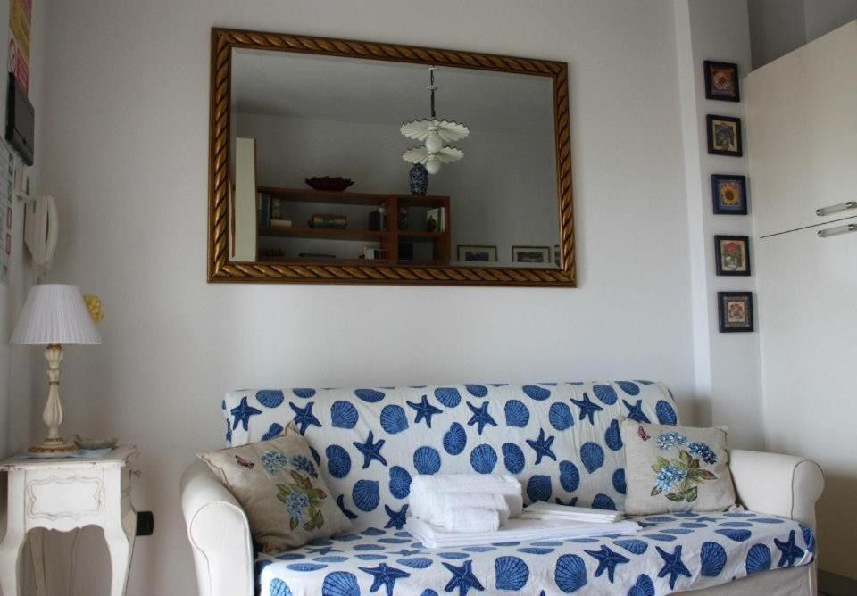 Soggiorno con pareti bianche, un divano con motivo a conchiglia blu, un grande specchio e un piccolo tavolino laterale.