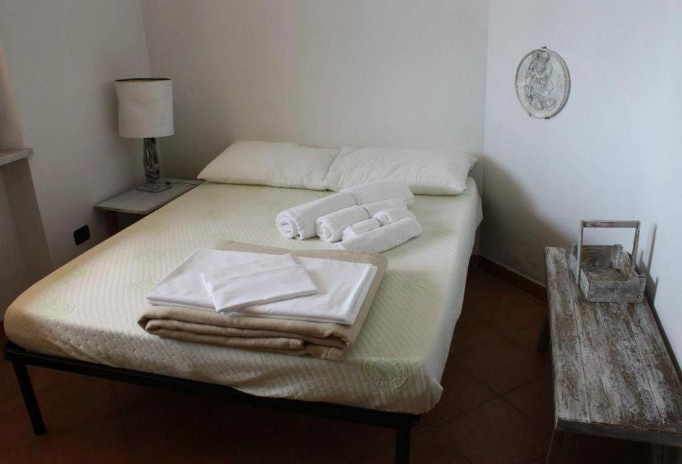 Camera da letto con letto matrimoniale, lampada da comodino e tavolino decorativo. Pareti bianche, pavimento marrone.